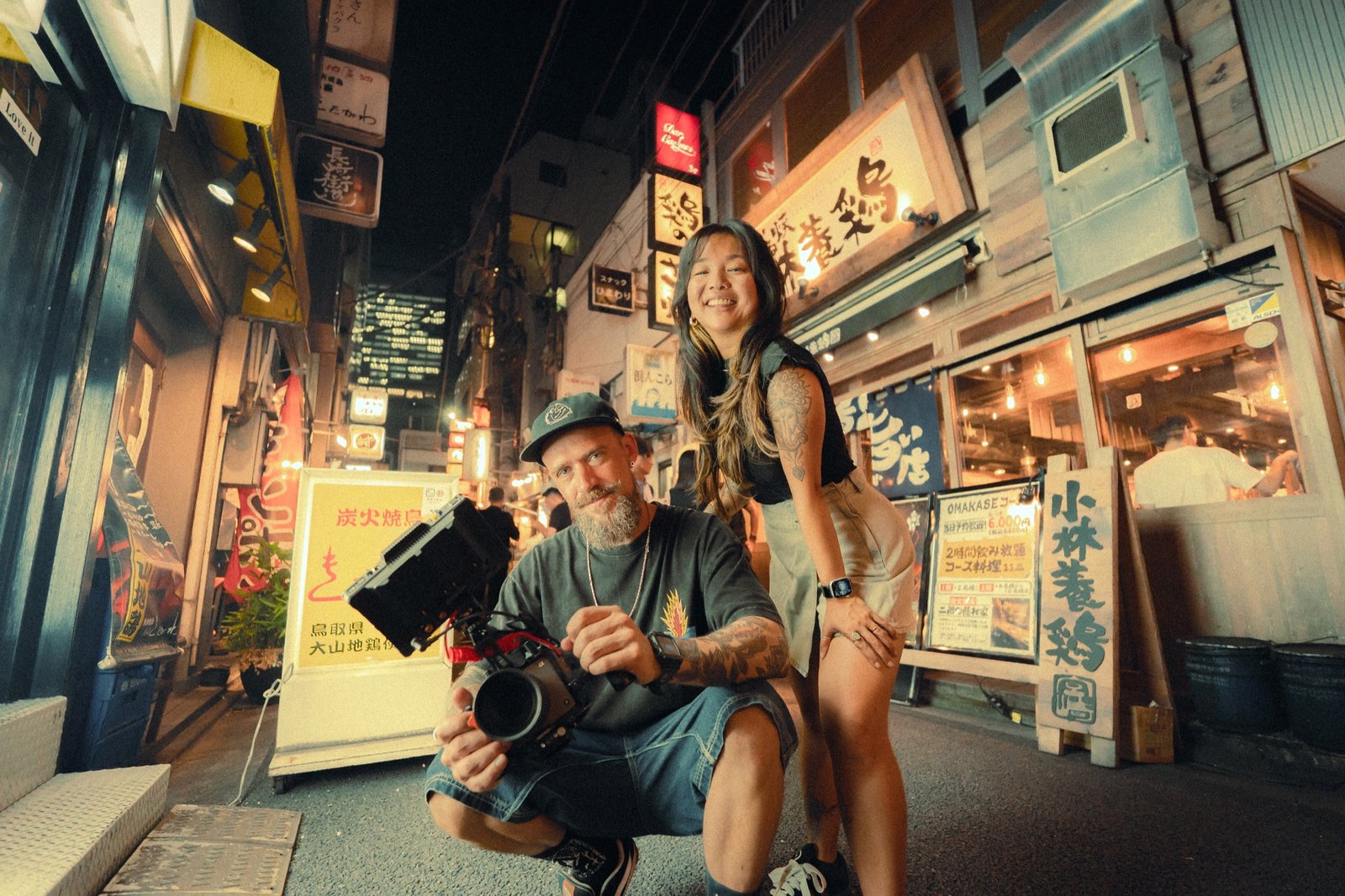 Aline e Junior, da NomadMakers, em uma rua iluminada do Japão com equipamento de filmagem